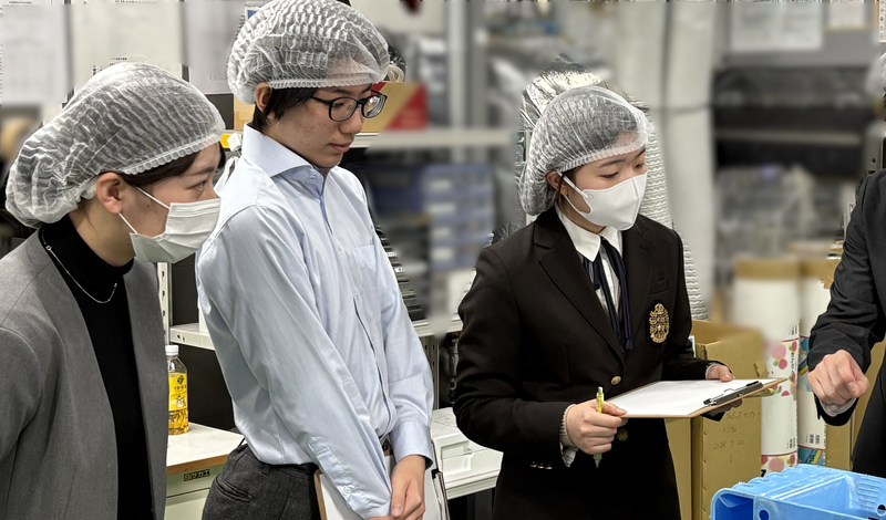 高校生が職場見学で社員から機械の説明を受けている様子
